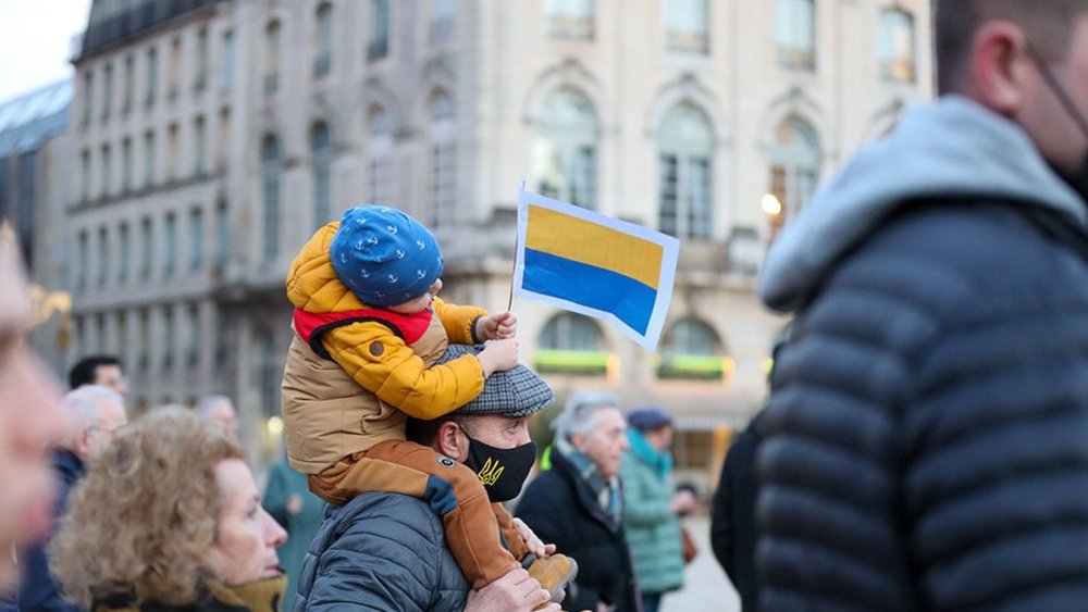 Un petit garçon sur les épaules de son père tient un drapeau Ukrainien lors d'une manifestation