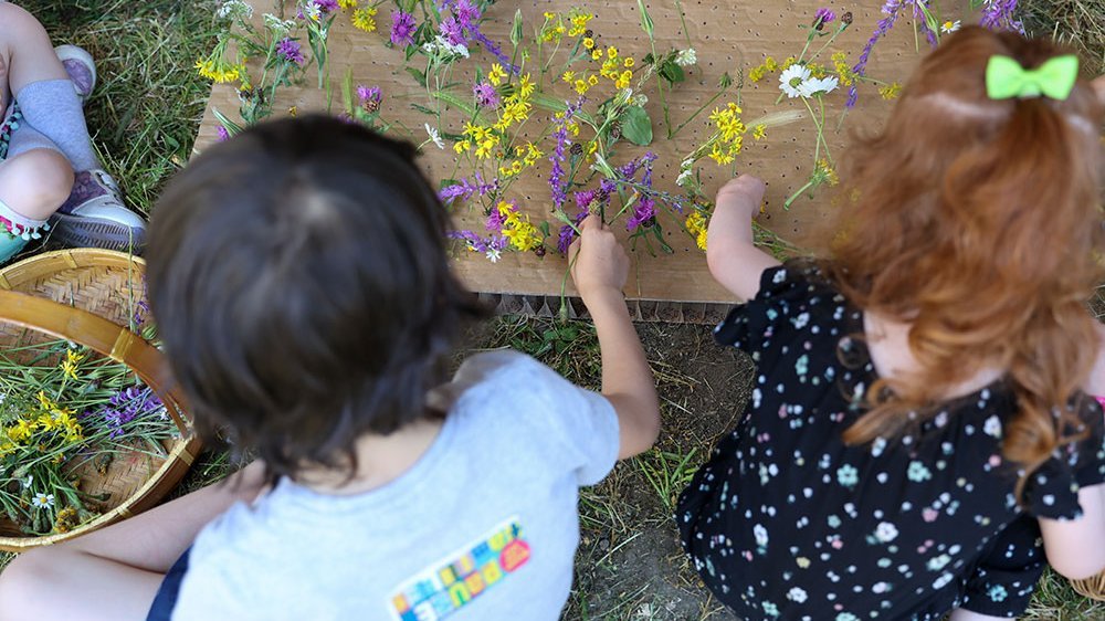 Deux fillettes assisens dans l'herbe tri des fleurs sur une table en carton